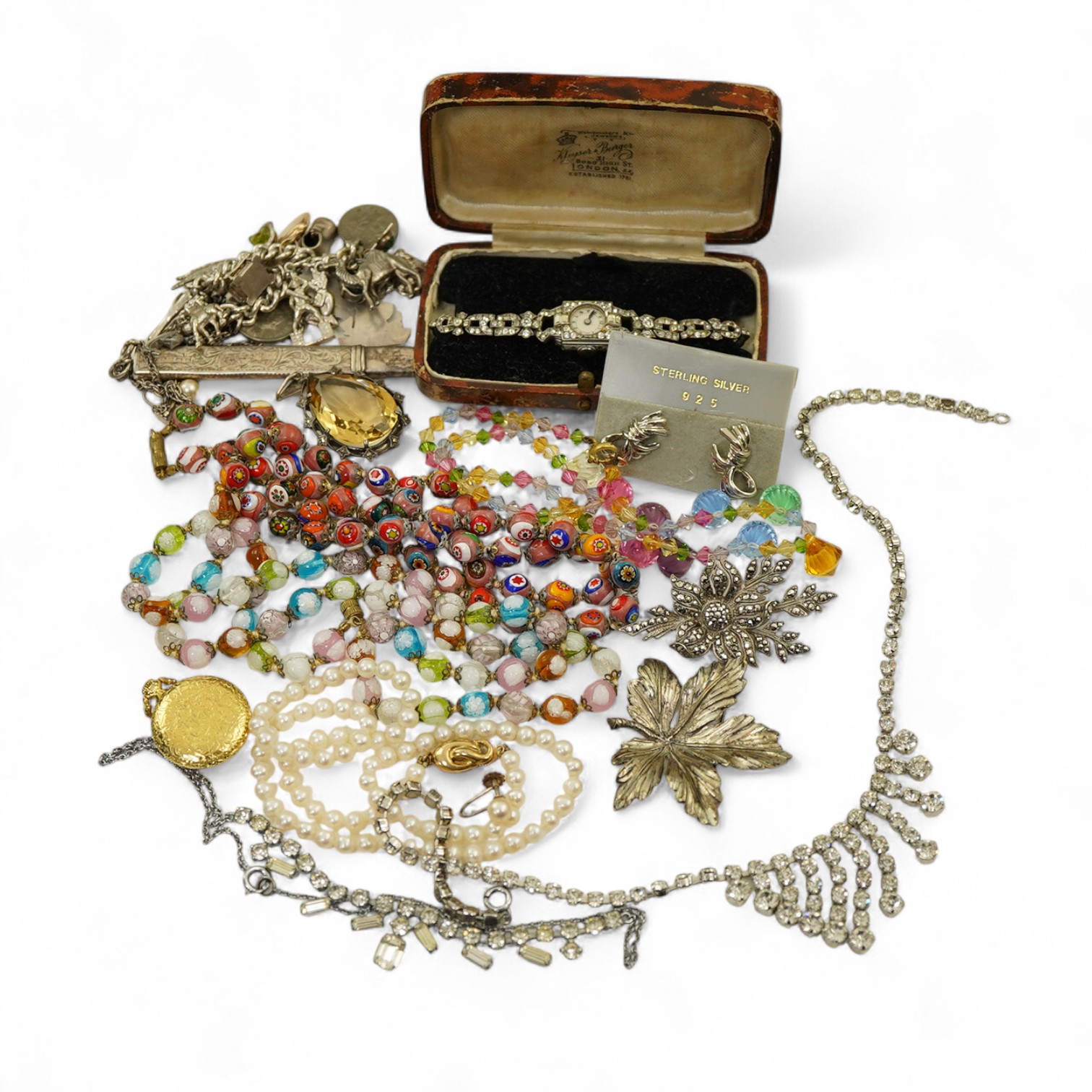 A collection of costume jewels, comprising: a charm bracelet suspending a series of charms, some in silver; a silver pencil; a sycamore leaf brooch; a pair of earrings of knotted design; an Art Deco paste watch; a gilt m